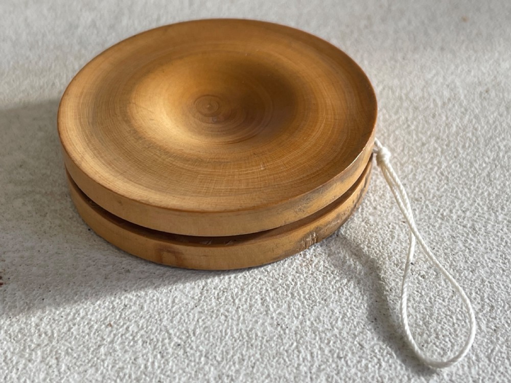 A lathe-turned boxwood yo-yo featuring dished concave sides and a tied white cotton cord.