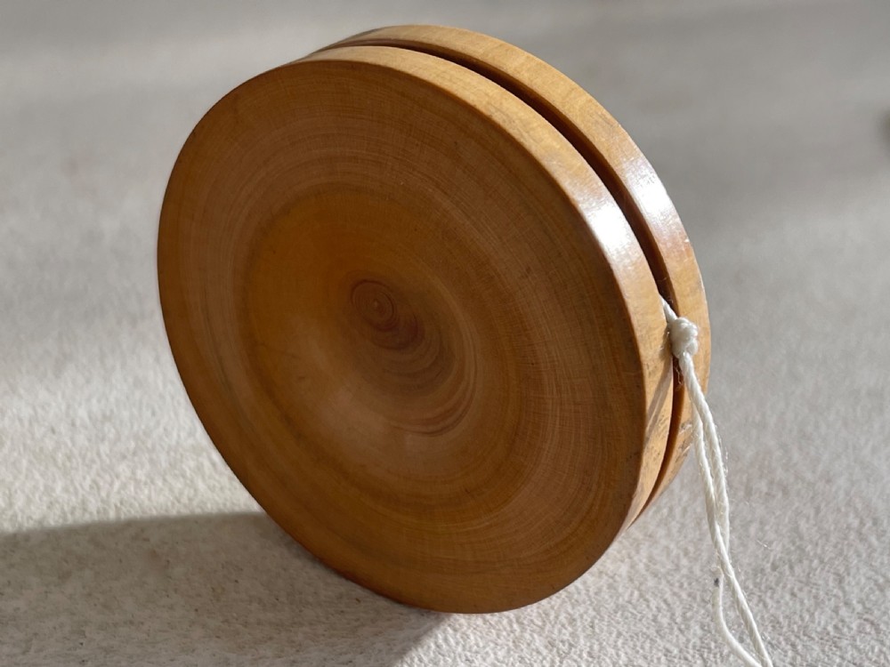 A lathe-turned boxwood yo-yo featuring dished concave sides and a tied white cotton cord. View II