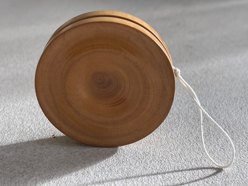 A lathe-turned boxwood yo-yo featuring dished concave sides and a tied white cotton cord. View III