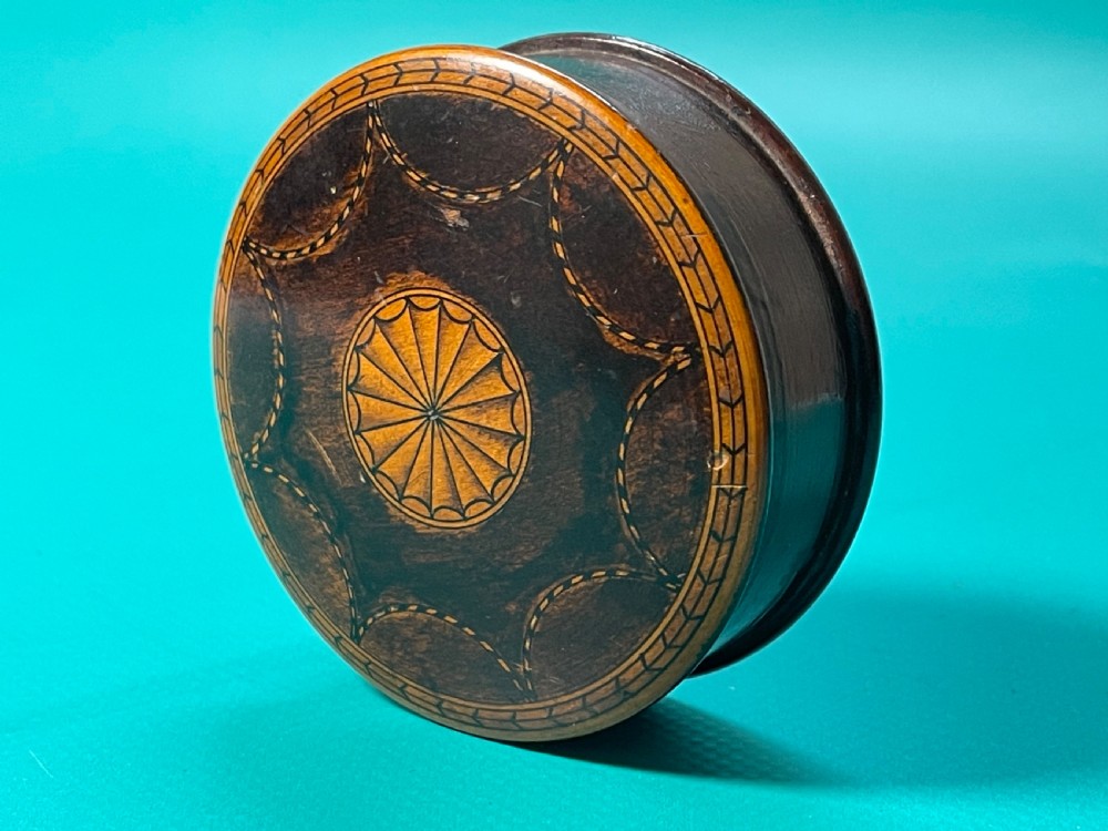 A circular Georgian wooden box featuring dark timber with light wood inlay forming a central rosette, scalloped pattern, and geometric border.