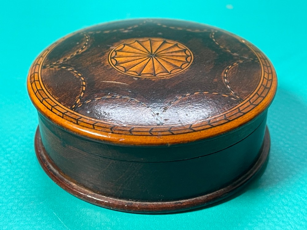 A circular Georgian wooden box featuring dark timber with light wood inlay forming a central rosette, scalloped pattern, and geometric border. View II