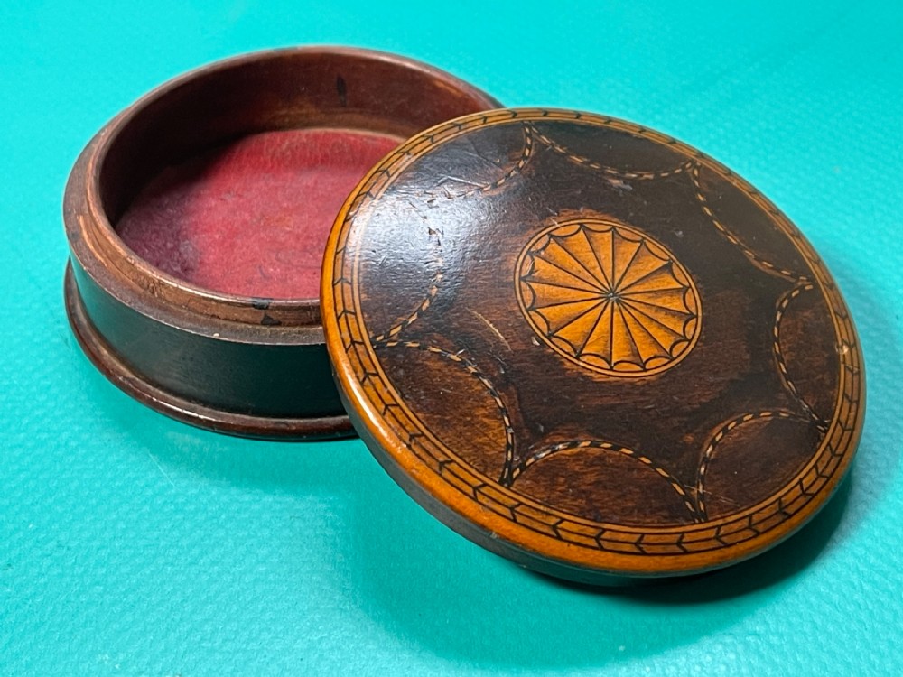A circular Georgian wooden box featuring dark timber with light wood inlay forming a central rosette, scalloped pattern, and geometric border. View III
