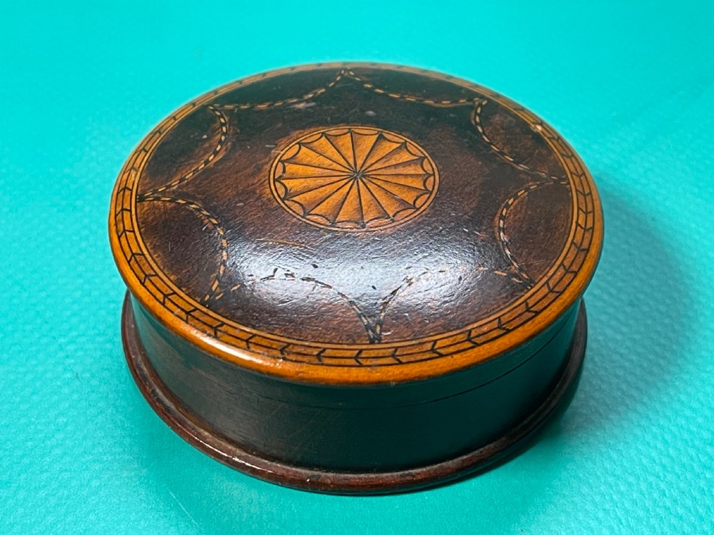 A circular Georgian wooden box featuring dark timber with light wood inlay forming a central rosette, scalloped pattern, and geometric border. View VII