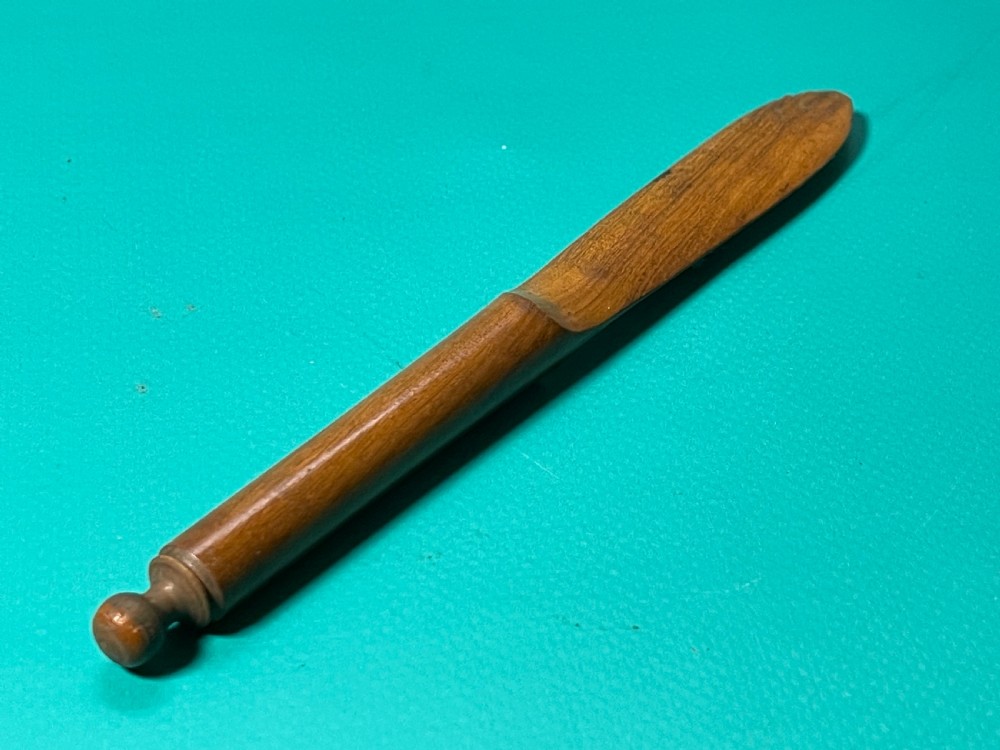 A turned and carved antique fruitwood letter opener with a rounded finial handle and a tapered blade, displayed on a green surface.