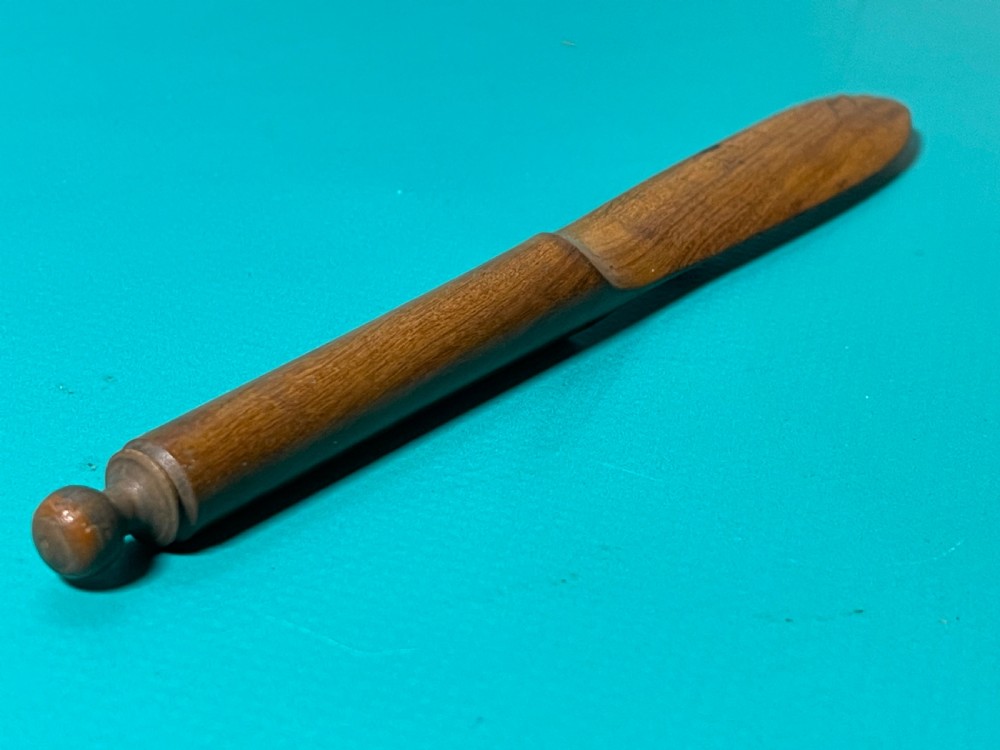 A turned and carved antique fruitwood letter opener with a rounded finial handle and a tapered blade, displayed on a green surface. View II
