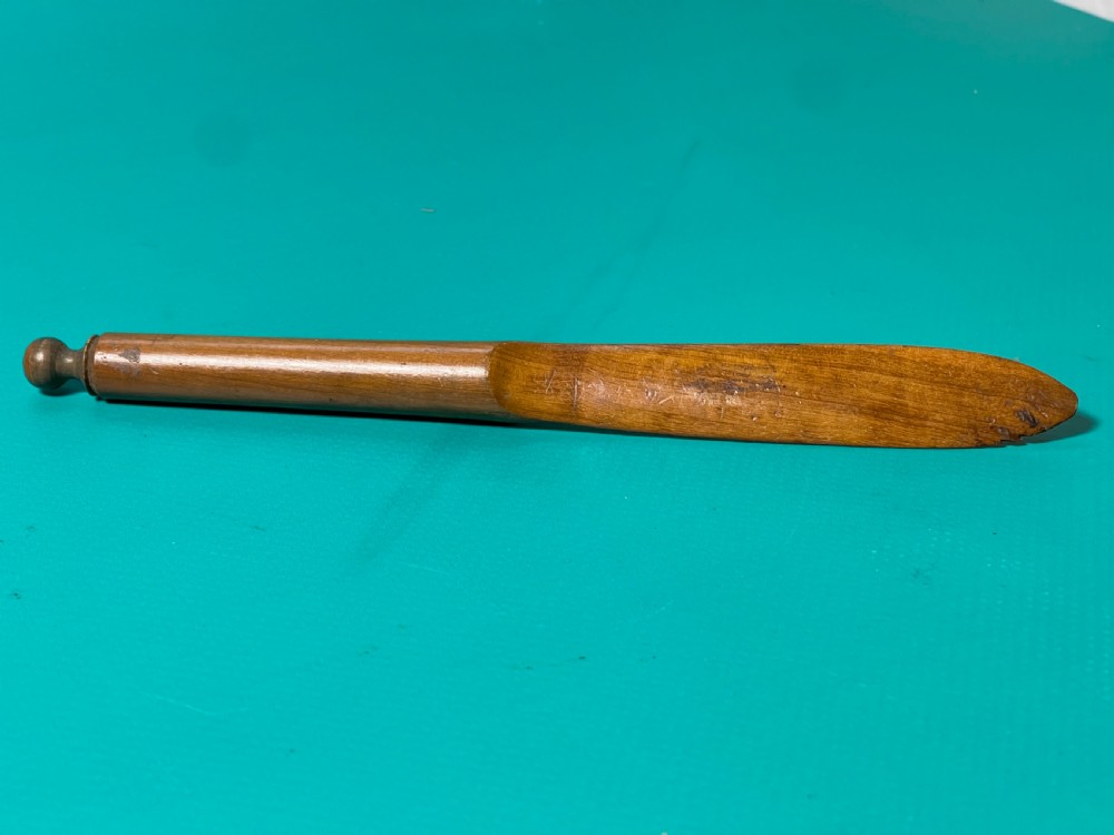 A turned and carved antique fruitwood letter opener with a rounded finial handle and a tapered blade, displayed on a green surface. View III