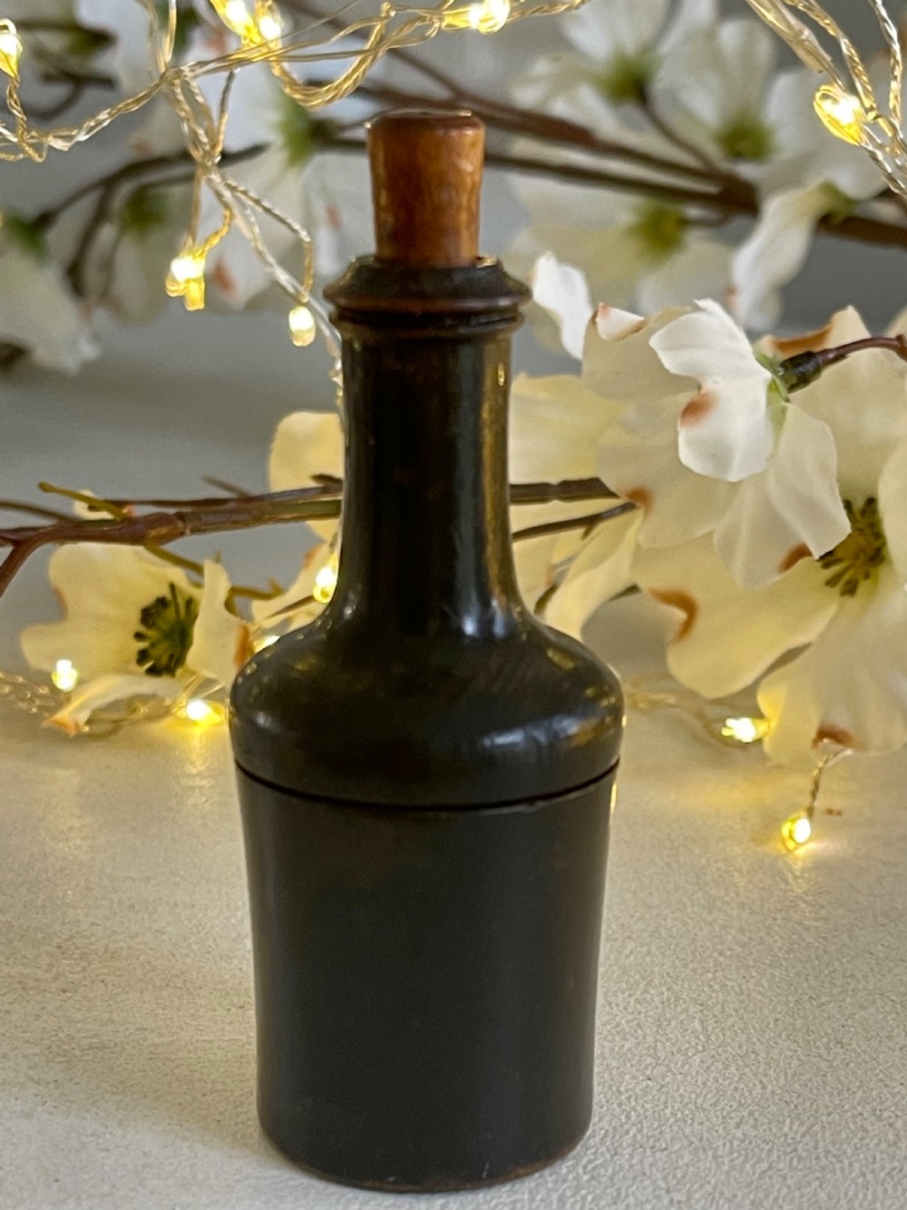 A small turned dark wood nutmeg grater shaped like a wine bottle with a wooden stopper top.