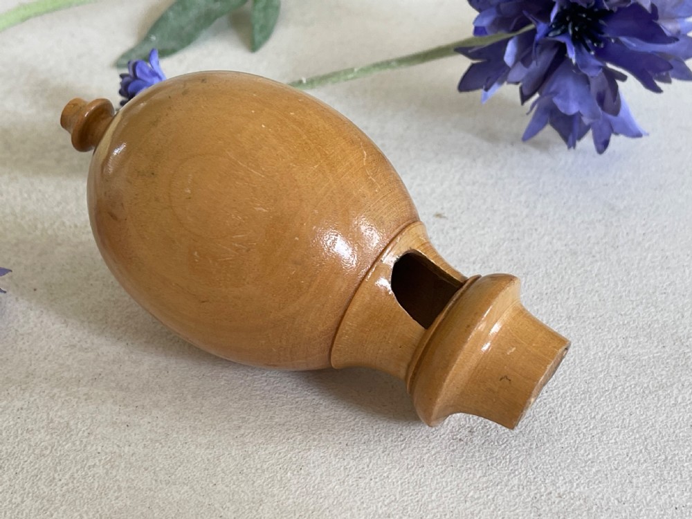A small turned wooden bird call with an egg-shaped body, a whistle mouth cut on one side, and shaped finials on each end.