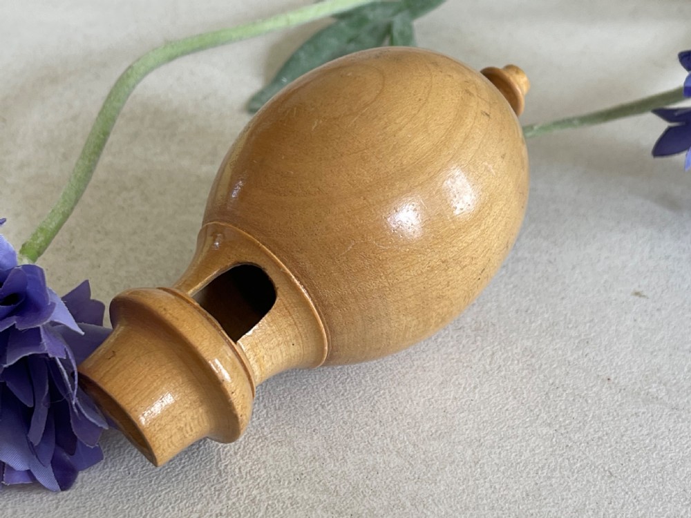 A small turned wooden bird call with an egg-shaped body, a whistle mouth cut on one side, and shaped finials on each end. View II