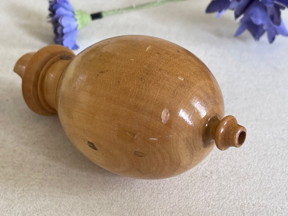 A small turned wooden bird call with an egg-shaped body, a whistle mouth cut on one side, and shaped finials on each end. View III