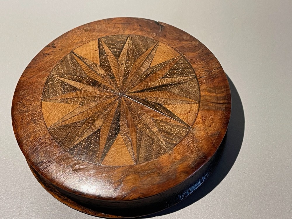 A small circular antique wooden snuff box featuring a central starburst inlaid pattern made from geometric specimen wood veneers. View III