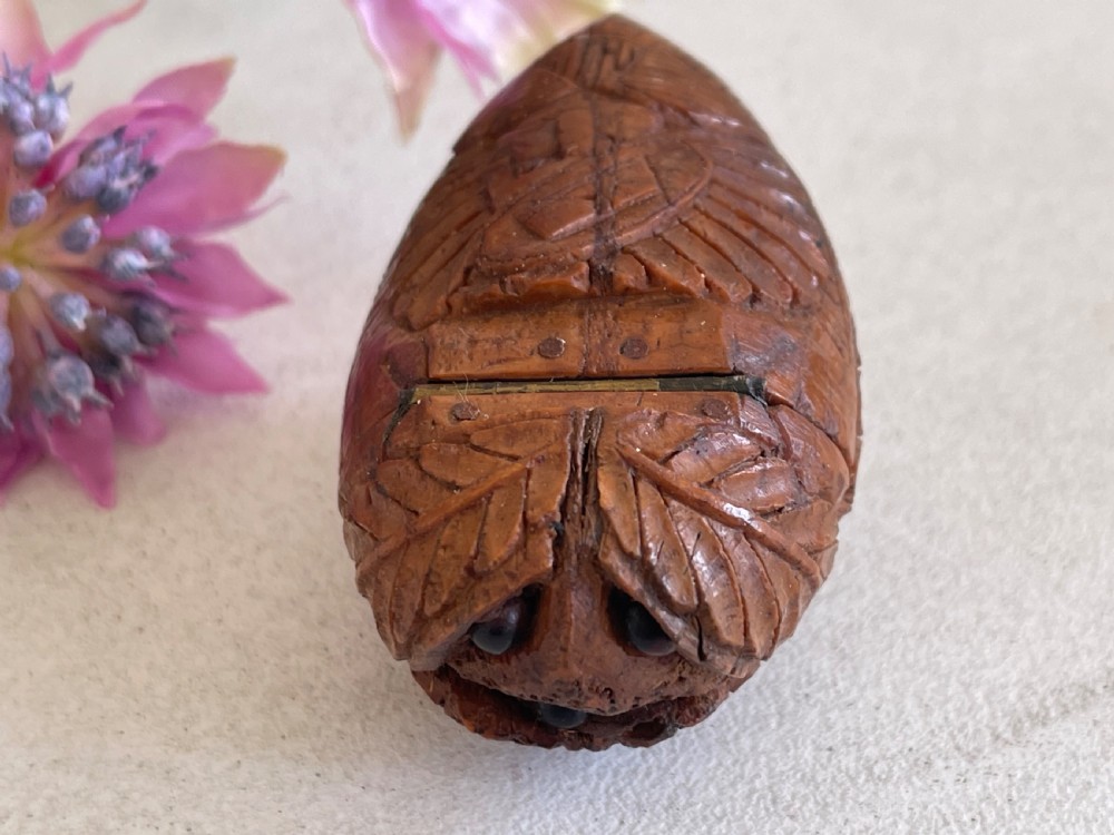 A small antique hand-carved coquilla nut snuff box shaped as a bugbear figure with detailed leaf engravings and a tiny metal hinge.
