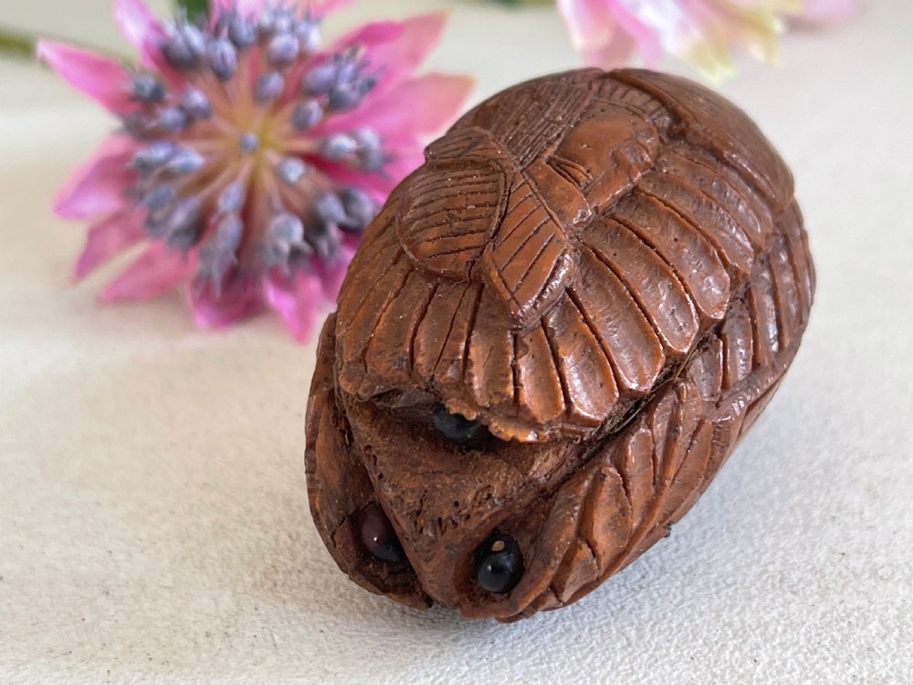 A small antique hand-carved coquilla nut snuff box shaped as a bugbear figure with detailed leaf engravings and a tiny metal hinge. View II