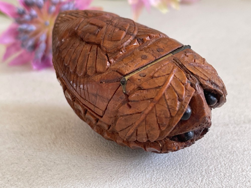 A small antique hand-carved coquilla nut snuff box shaped as a bugbear figure with detailed leaf engravings and a tiny metal hinge. View IV