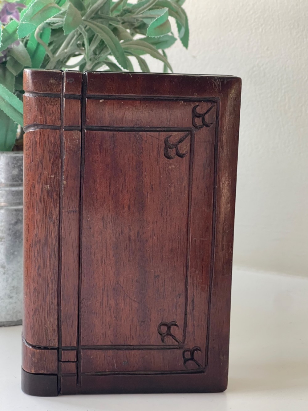 A dark brown carved wooden box designed in the shape of a book with decorative corner engravings.