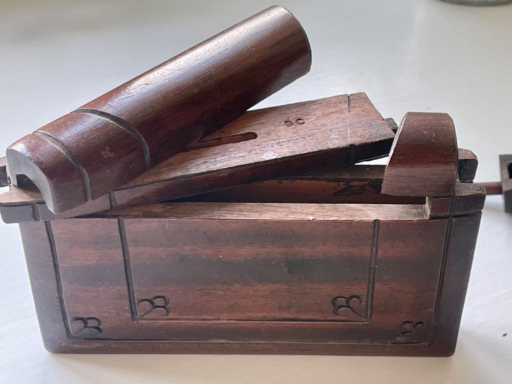 A dark brown carved wooden box designed in the shape of a book with decorative corner engravings. View IV