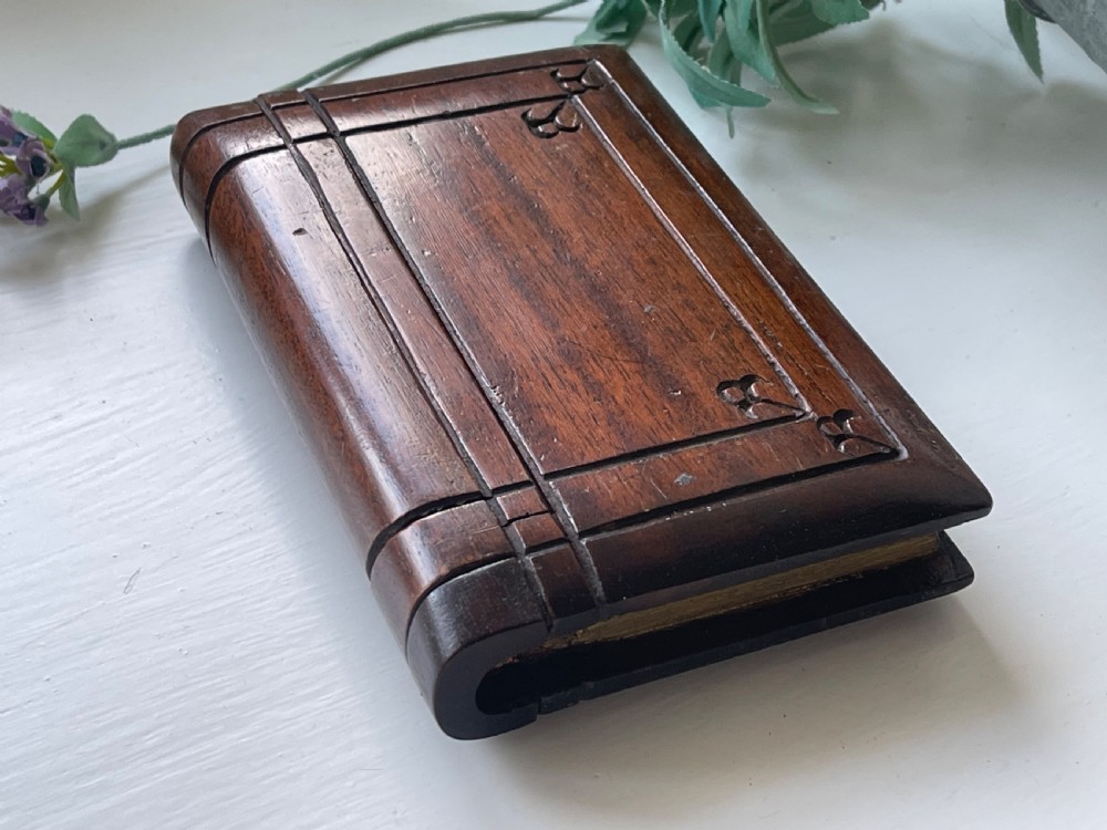 A dark brown carved wooden box designed in the shape of a book with decorative corner engravings. View V