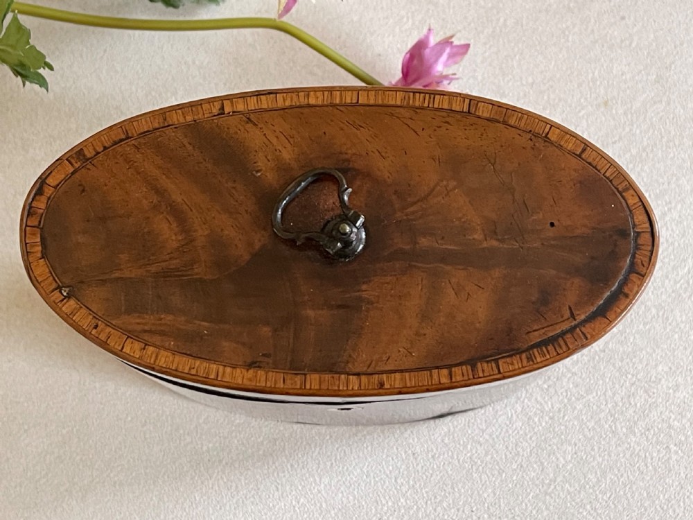 An eighteenth-century Georgian oval mahogany tea caddy featuring polished grain, a bone keyhole escutcheon, and a brass ring handle on the hinged top. View IV