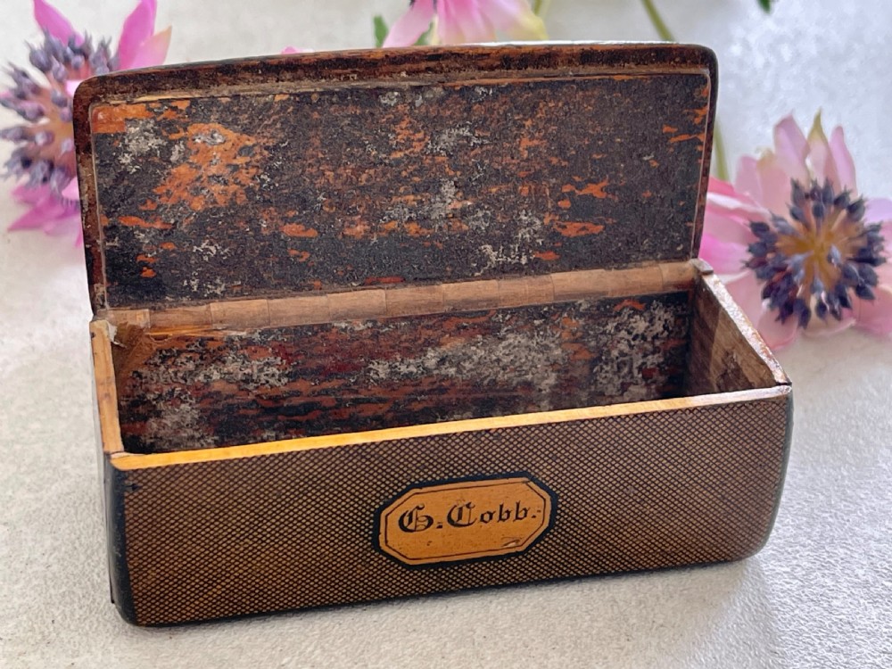 A small rectangular antique wooden snuff box featuring penwork illustrations of men in a tavern on the lid and a central name tag inscribed G. Cobb on the front. View III
