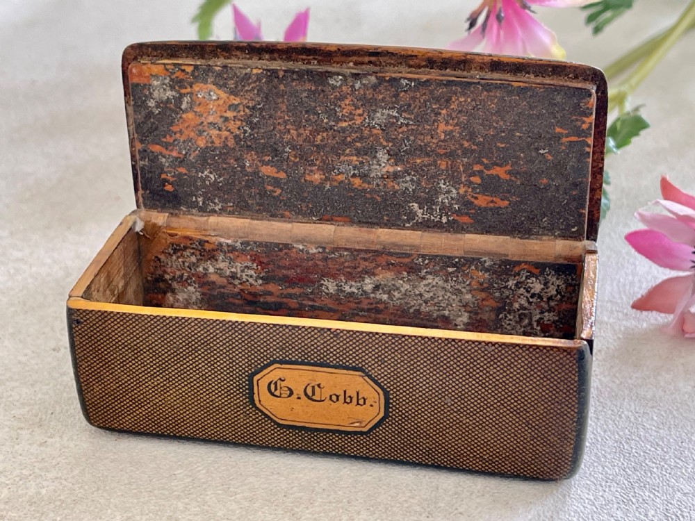 A small rectangular antique wooden snuff box featuring penwork illustrations of men in a tavern on the lid and a central name tag inscribed G. Cobb on the front. View VIII