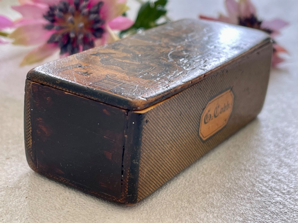 A small rectangular antique wooden snuff box featuring penwork illustrations of men in a tavern on the lid and a central name tag inscribed G. Cobb on the front. View IX