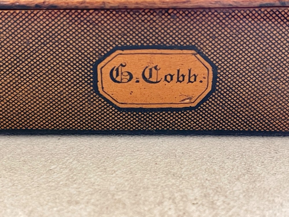 A small rectangular antique wooden snuff box featuring penwork illustrations of men in a tavern on the lid and a central name tag inscribed G. Cobb on the front. View X