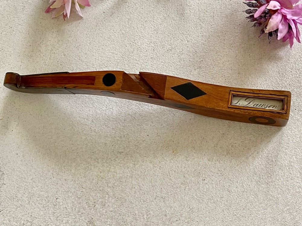 A curved antique wooden knitting sheath featuring geometric marquetry inlays and a small metal-ended aperture. View V