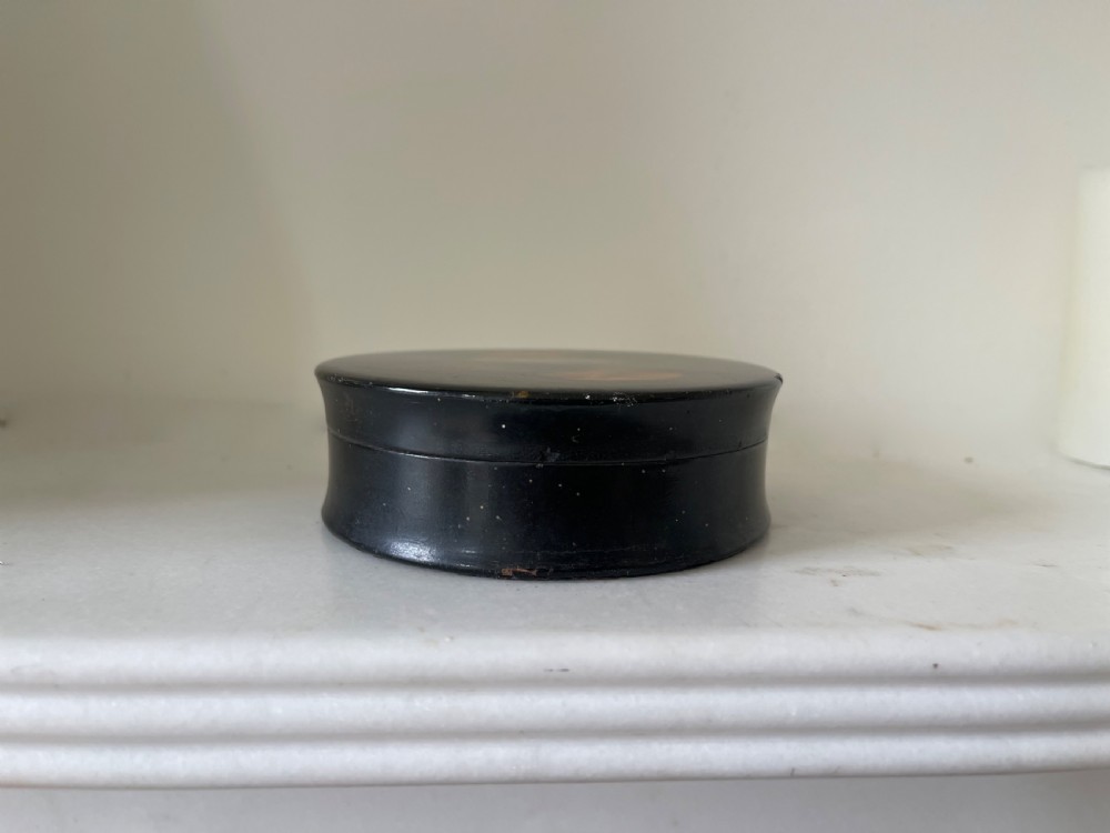 A circular black lacquered papier-mache snuff box lid featuring a hand-painted classical portrait of a bearded man wearing a green headband. View III