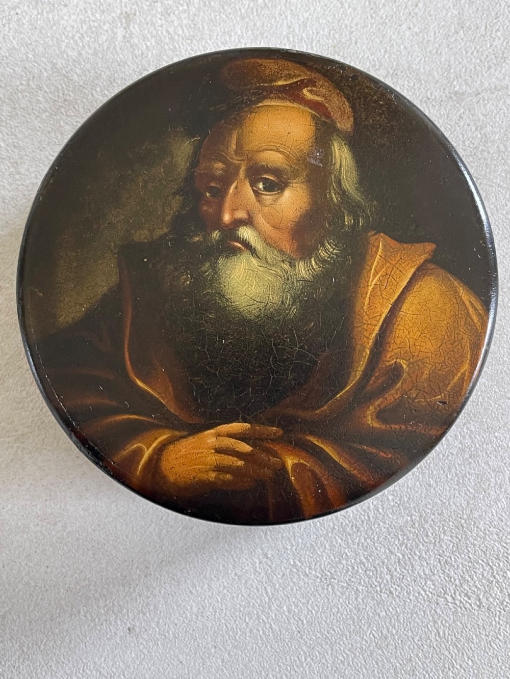 A circular dark brown antique papier-mache snuff box featuring a detailed painted miniature portrait of a bearded man on the lid. View V
