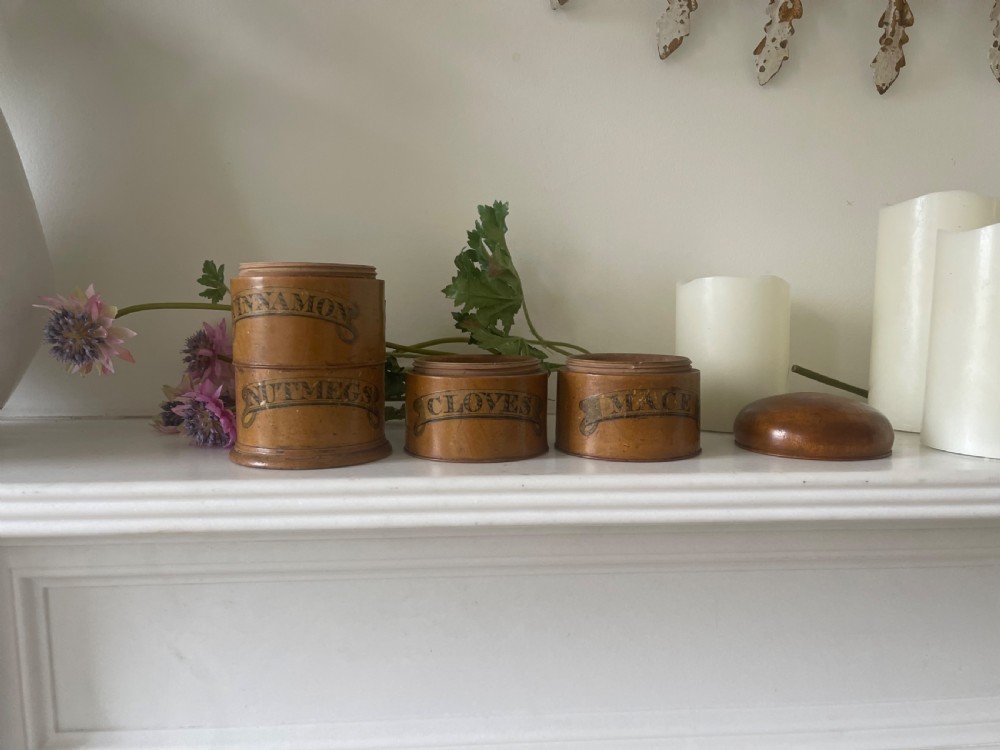 A four-tier turned wooden spice tower featuring black printed banner labels reading Mace, Cloves, Cinnamon, and Nutmegs. View IV
