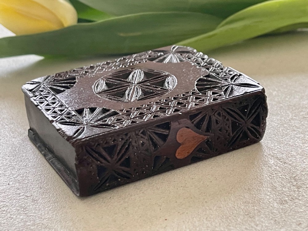 A dark brown chip-carved wooden snuff box shaped like a miniature book with geometric star carvings and a light wood heart inlay on the spine.