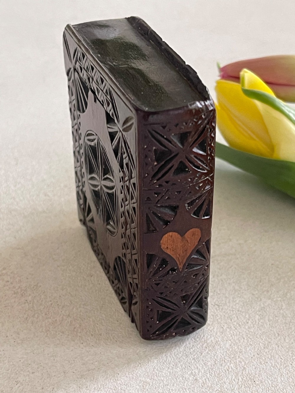 A dark brown chip-carved wooden snuff box shaped like a miniature book with geometric star carvings and a light wood heart inlay on the spine. View II