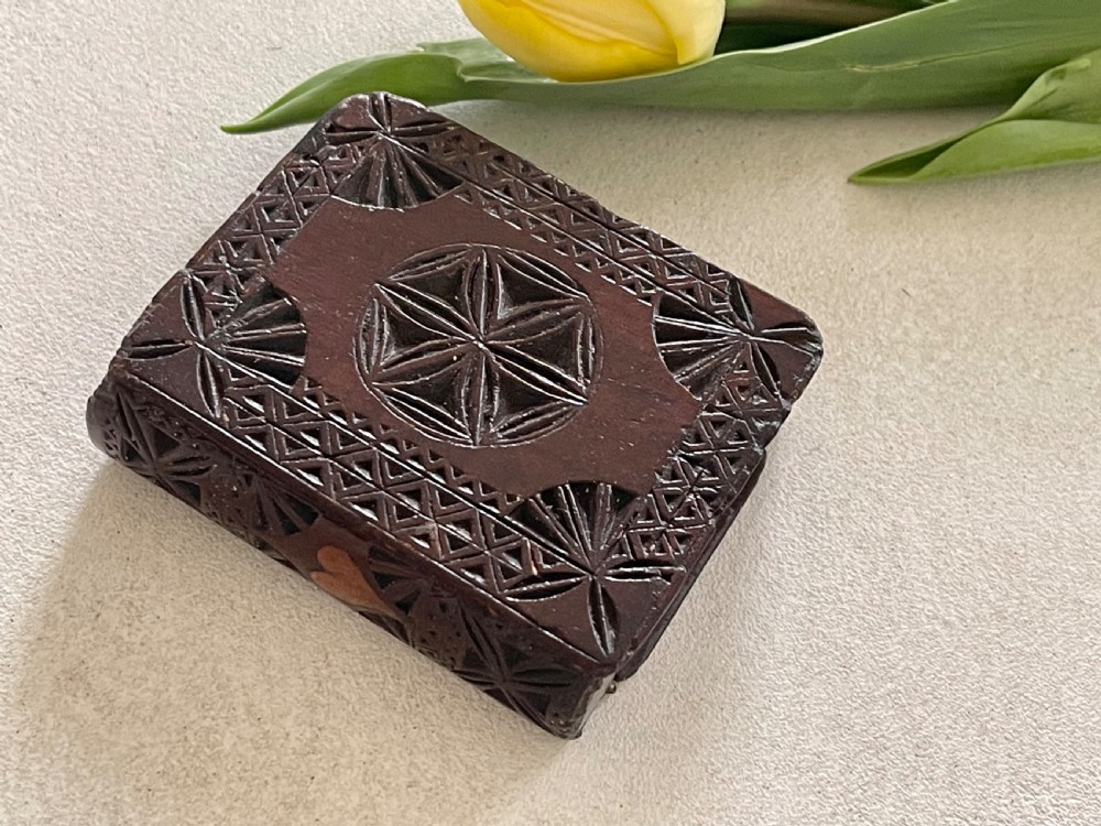A dark brown chip-carved wooden snuff box shaped like a miniature book with geometric star carvings and a light wood heart inlay on the spine. View V
