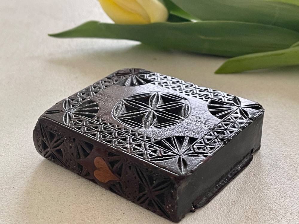 A dark brown chip-carved wooden snuff box shaped like a miniature book with geometric star carvings and a light wood heart inlay on the spine. View VII