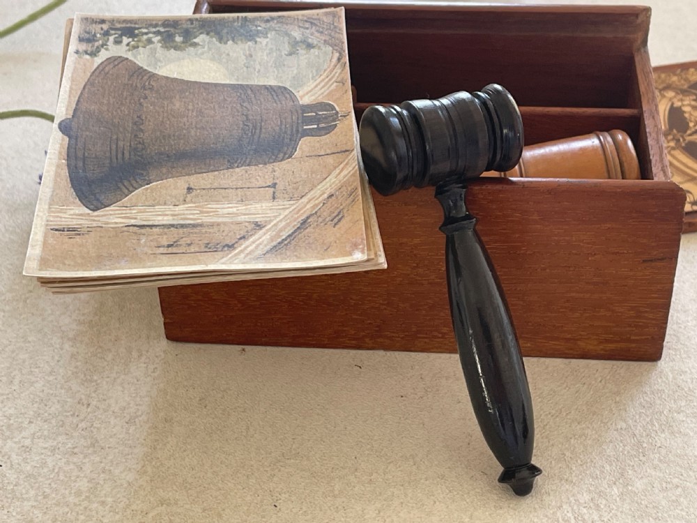 A rectangular wooden game box with a detailed printed paper lid depicting a bell, a hammer, floral garlands, and classical scrollwork. View II