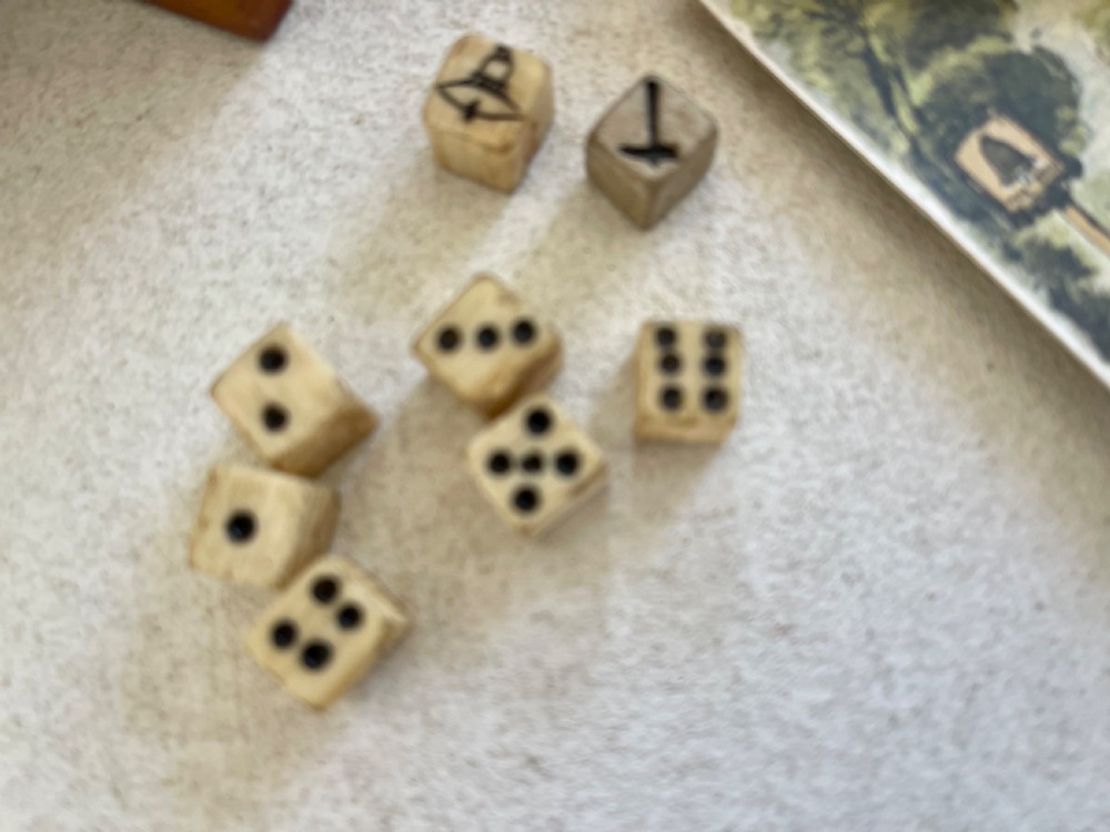 A rectangular wooden game box with a detailed printed paper lid depicting a bell, a hammer, floral garlands, and classical scrollwork. View V
