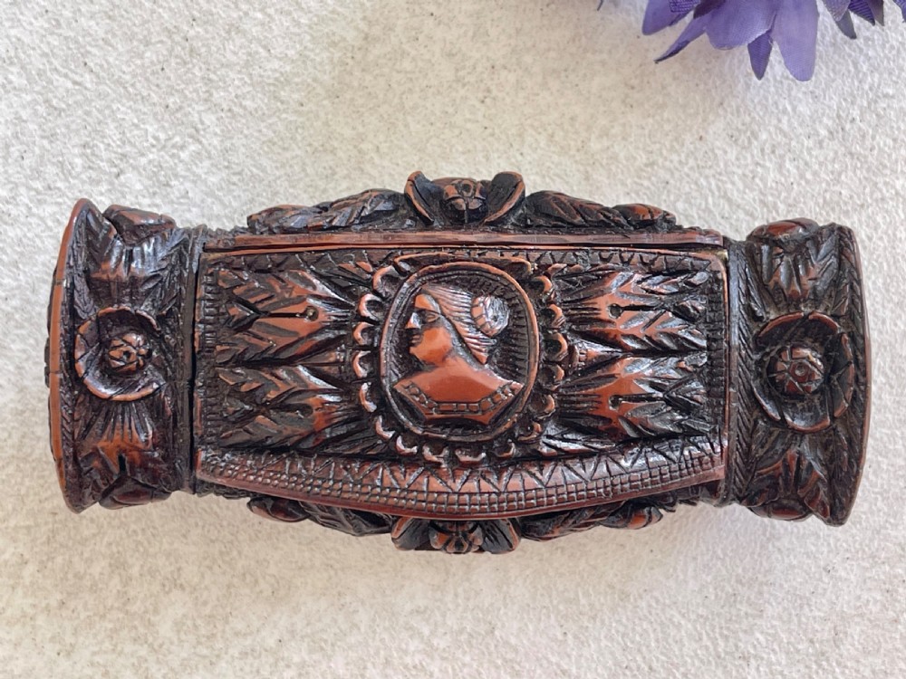 A detailed carved dark brown coquilla nut snuff box featuring a central relief medallion of a female profile surrounded by decorative foliage patterns.
