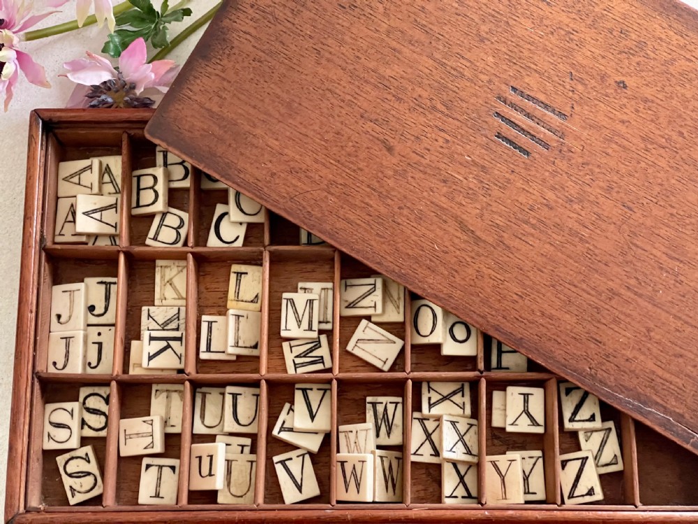 A Victorian mahogany alphabet box shown partially open, revealing a grid of compartments holding bone tiles with printed capital letters.