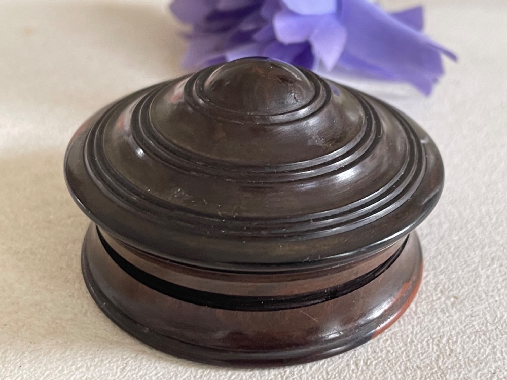 A small, circular antique turned wood case with a domed, stepped lid designed to hold a travelling compass sundial.