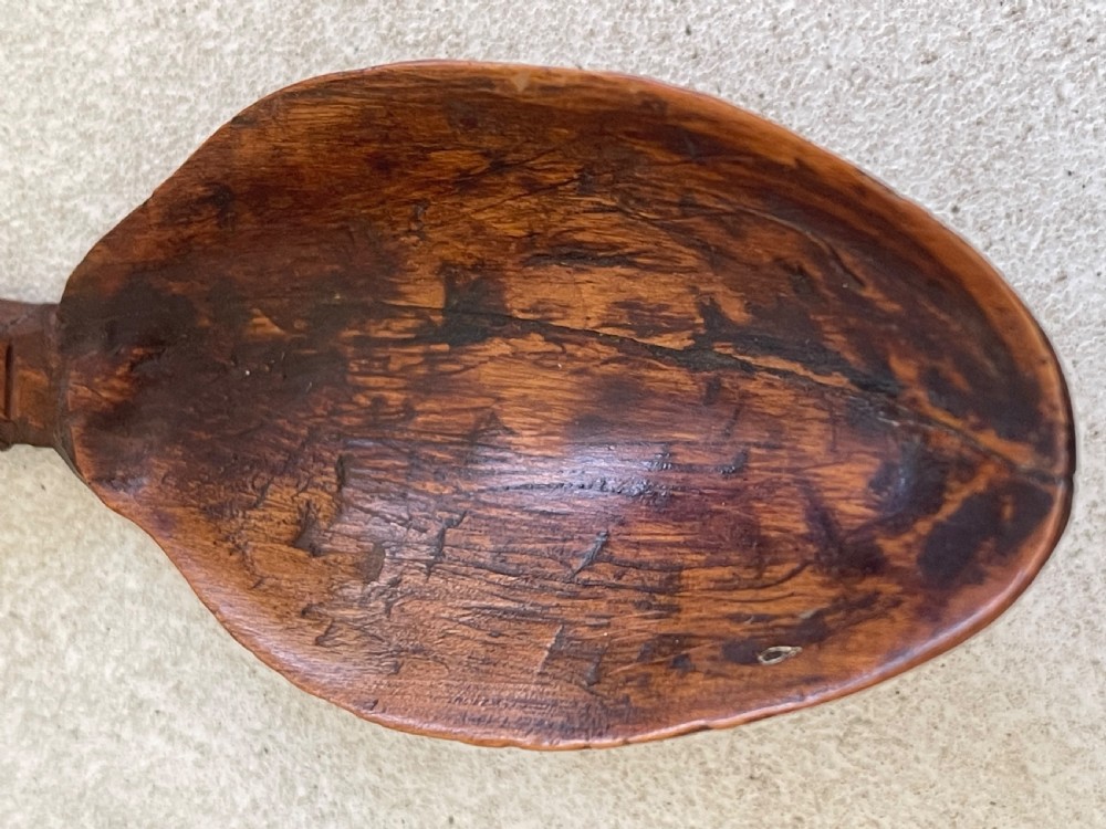 A hand-carved dark wood Welsh lovespoon with geometric chip-carved detailing, a pierced heart cutout at the top, and a smoothed spoon bowl. View III