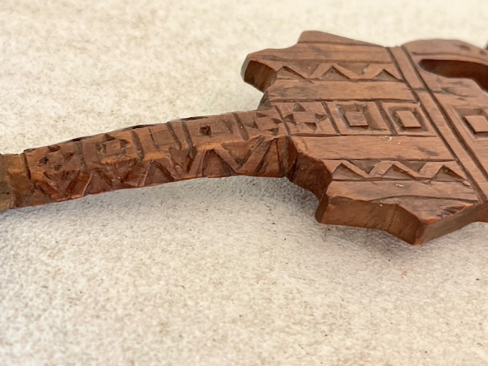 A hand-carved dark wood Welsh lovespoon with geometric chip-carved detailing, a pierced heart cutout at the top, and a smoothed spoon bowl. View V