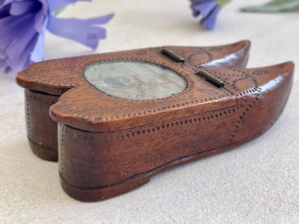 A carved brown wooden double shoe-shaped snuff box featuring stippled geometric patterns, metal spring hinges, and an inset oval miniature portrait of a lady on top.