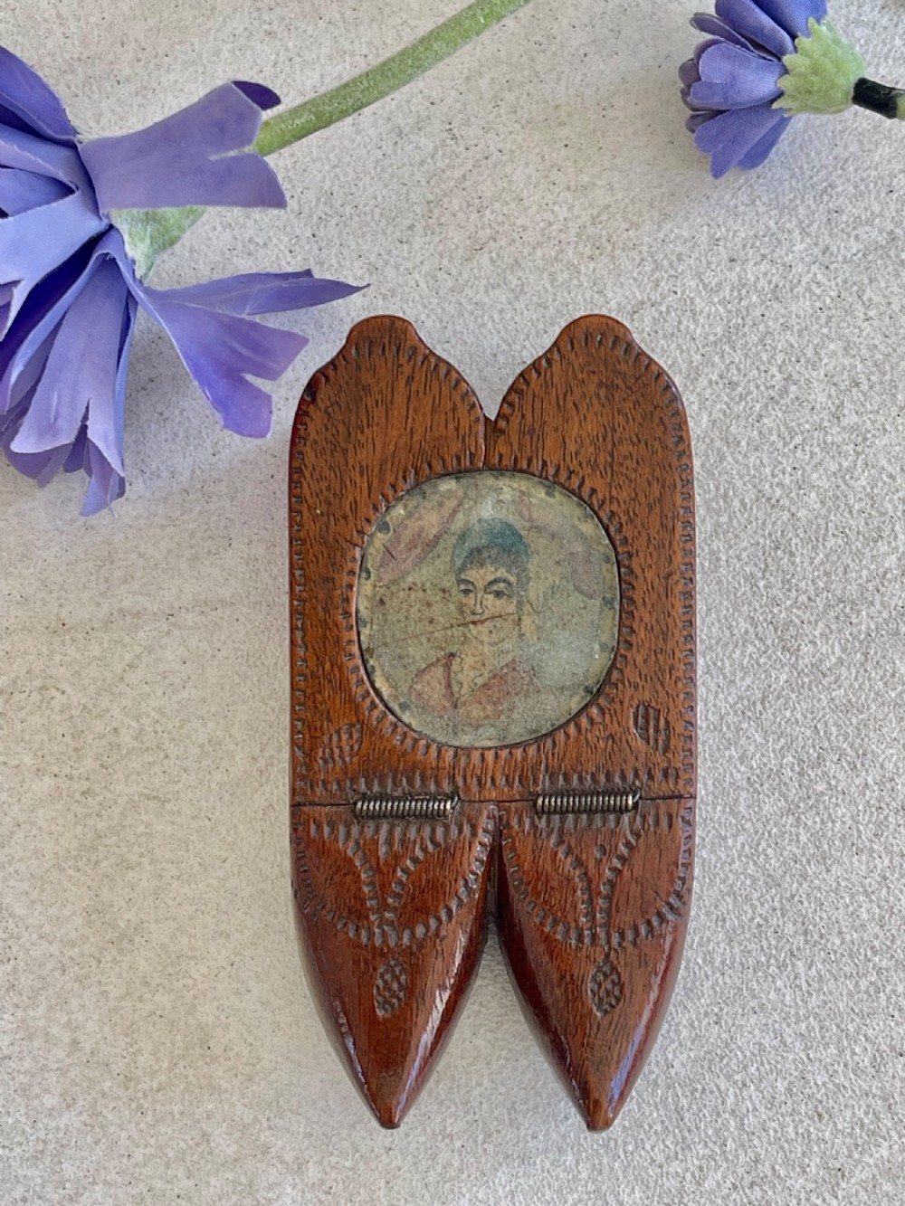 A carved brown wooden double shoe-shaped snuff box featuring stippled geometric patterns, metal spring hinges, and an inset oval miniature portrait of a lady on top. View IV