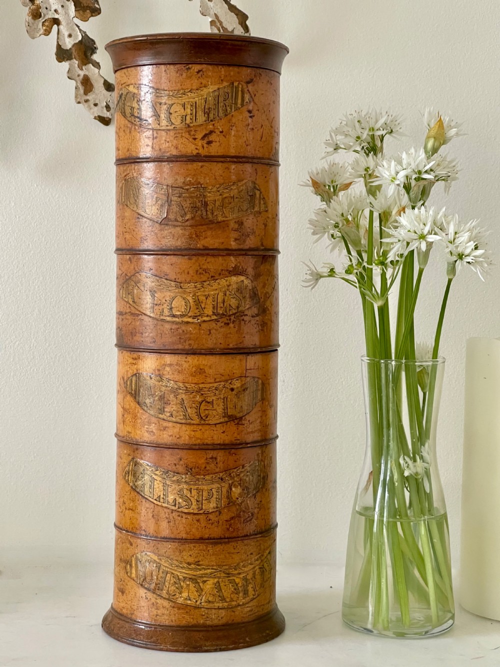 A tall, lathe-turned wooden six-tier cylindrical spice tower featuring original paper labels on each section.