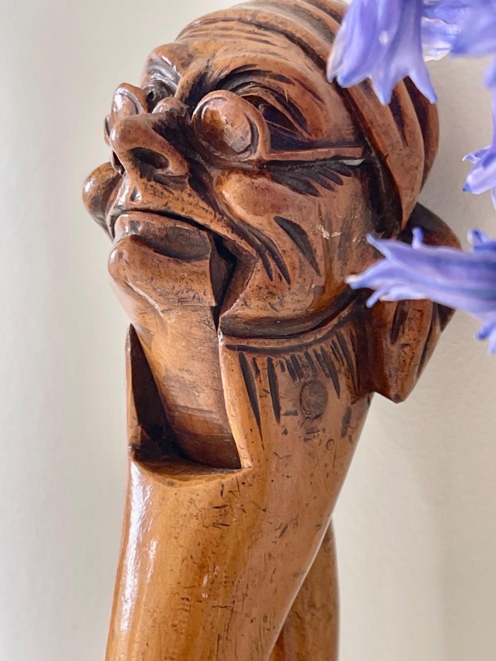A hand-carved wooden lever nutcracker sculpted into a human head wearing spectacles and a soft cap. View II