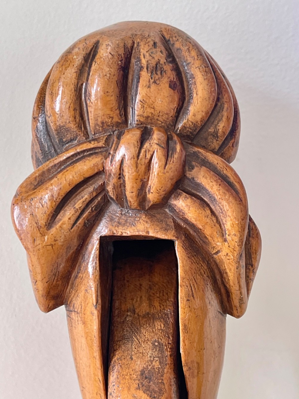 A hand-carved wooden lever nutcracker sculpted into a human head wearing spectacles and a soft cap. View IV