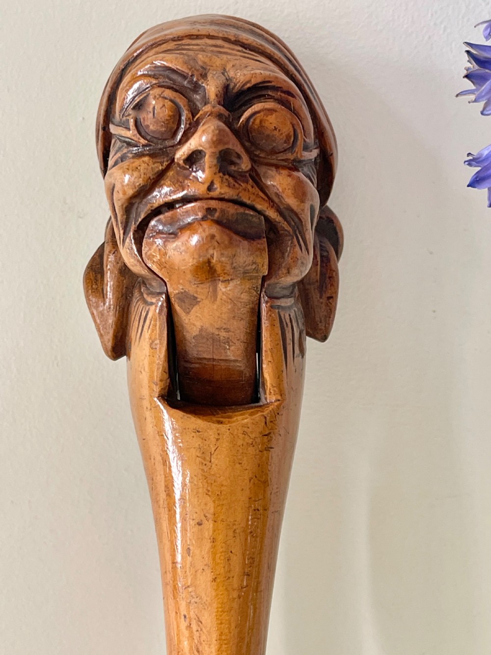 A hand-carved wooden lever nutcracker sculpted into a human head wearing spectacles and a soft cap. View VI