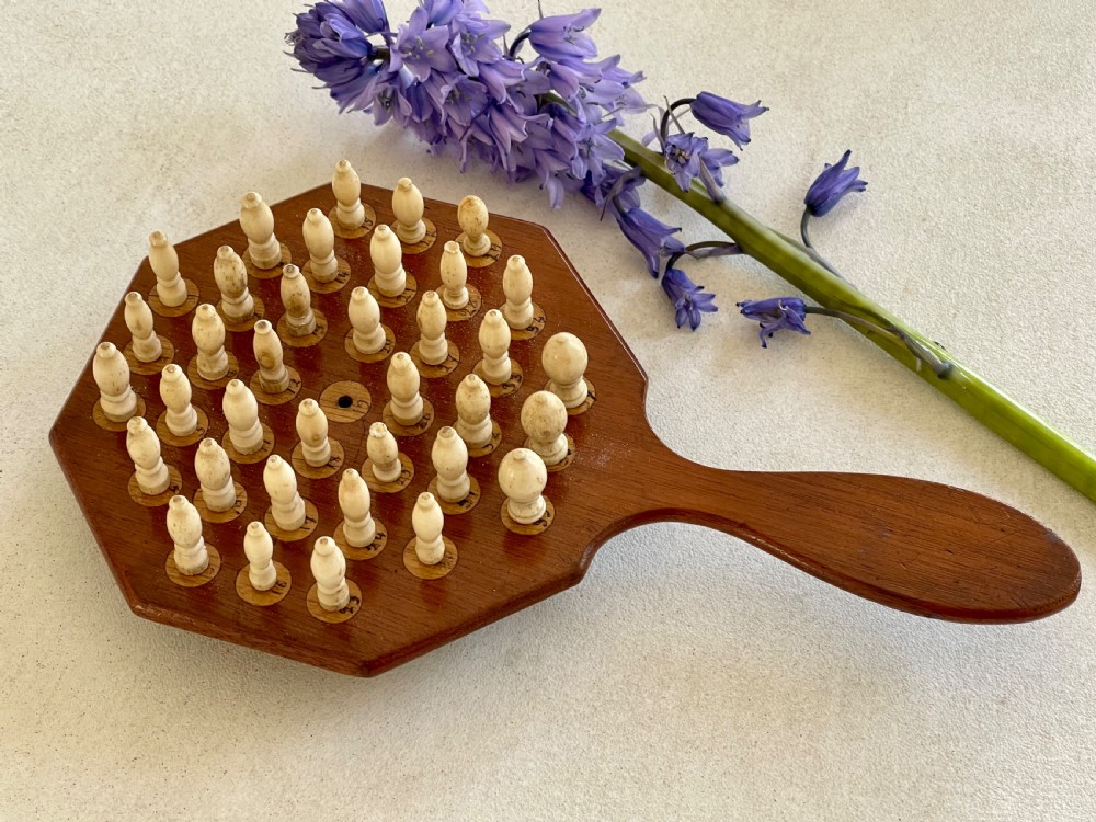 A paddle-shaped wooden peg solitaire board featuring numbered slots and carved bone pegs.