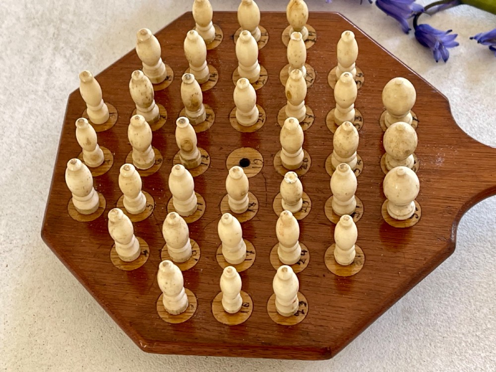 A paddle-shaped wooden peg solitaire board featuring numbered slots and carved bone pegs. View II