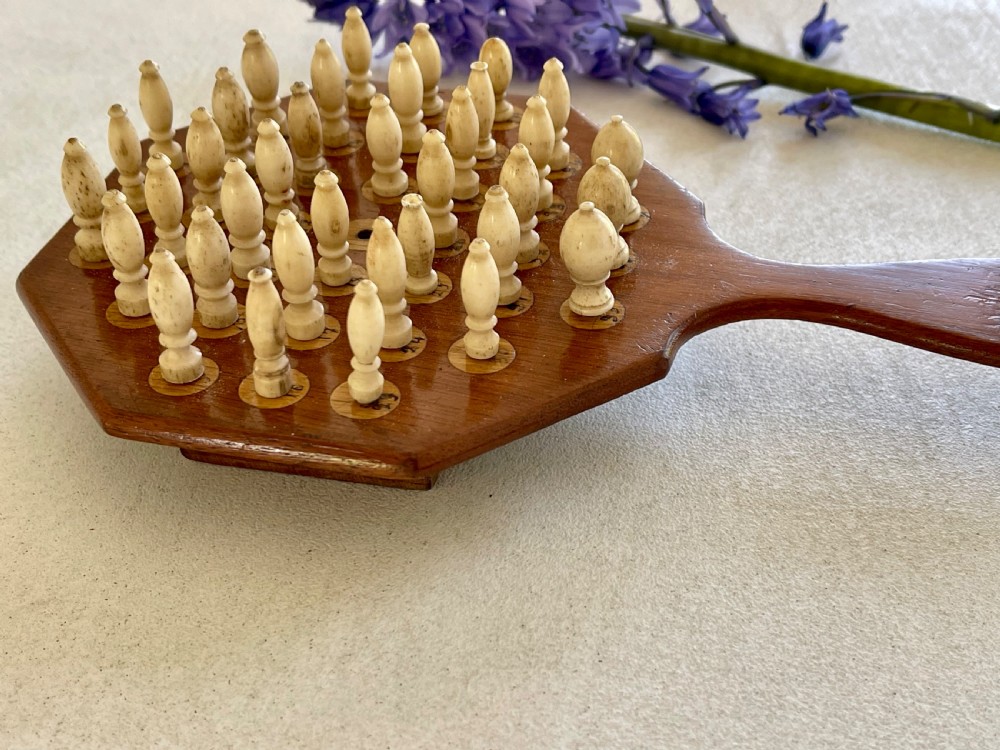 A paddle-shaped wooden peg solitaire board featuring numbered slots and carved bone pegs. View III